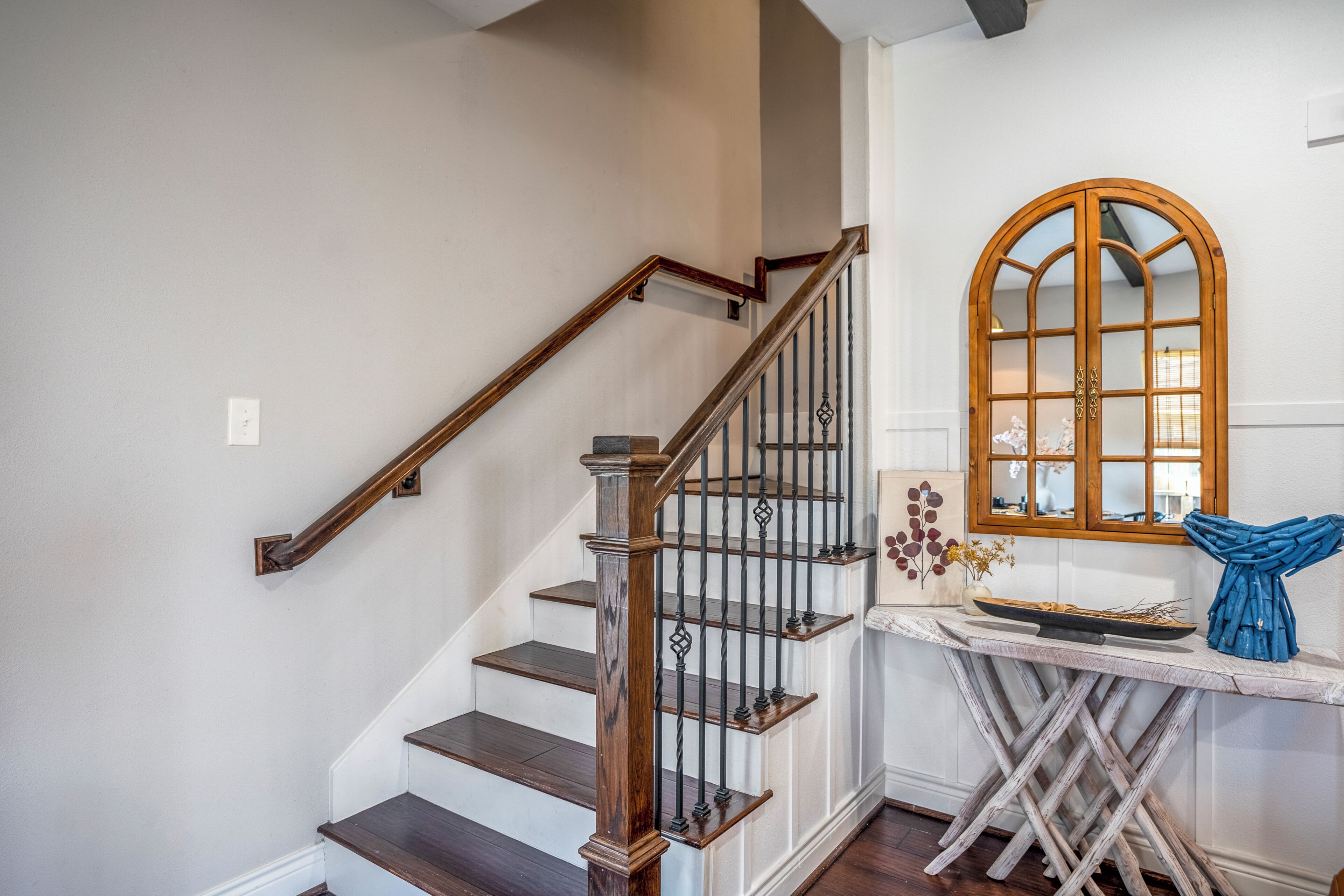 Una escalera con barandillas de madera y una pared blanca con un ventanal decorativo.