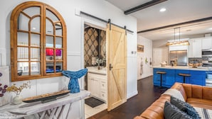 A modern kitchen with a central island, a sliding barn door, and a cozy living area with a leather sofa. - Empress Garden Villa (Houston)