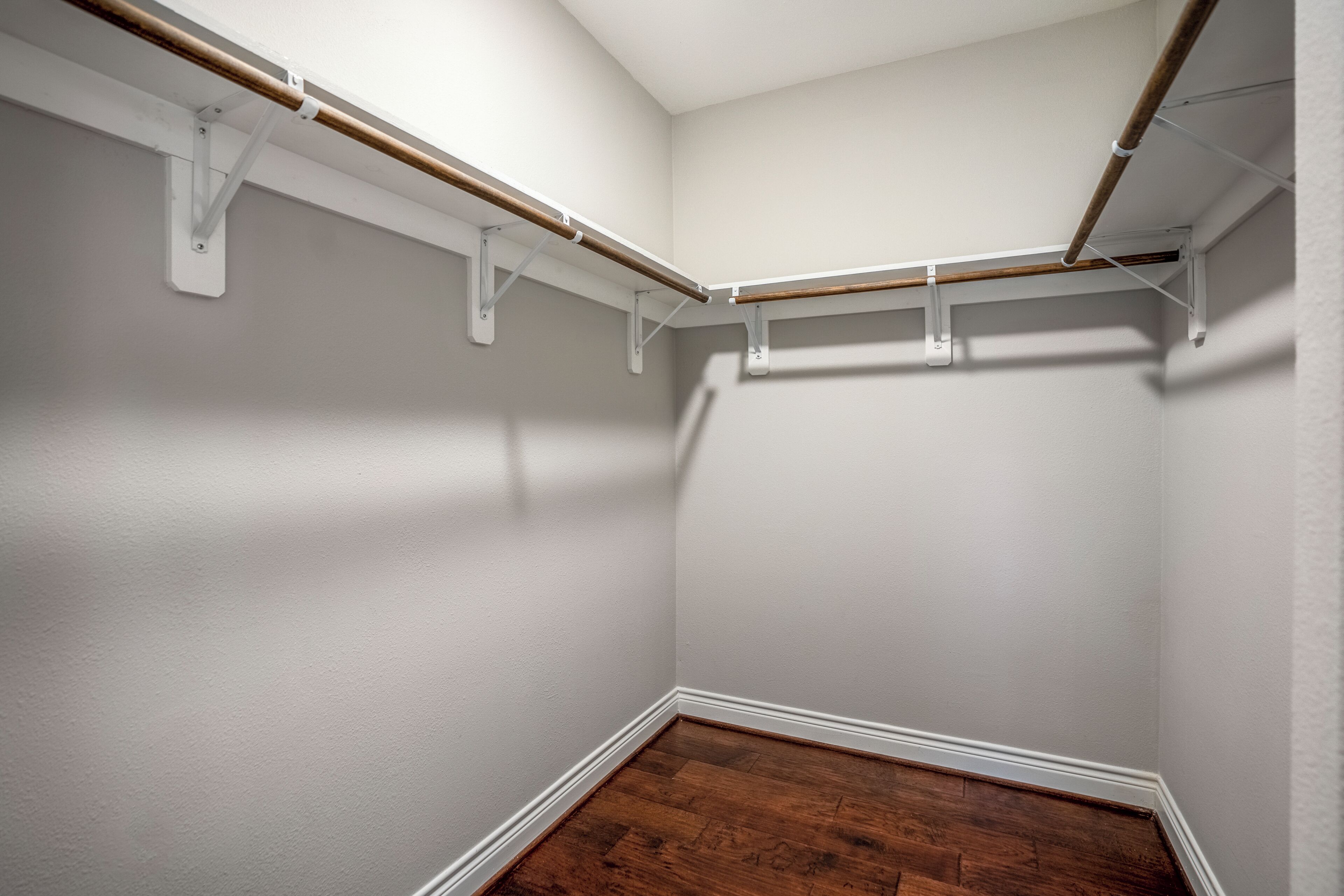 A corner closet with white walls, wooden flooring, and metal shelving units.