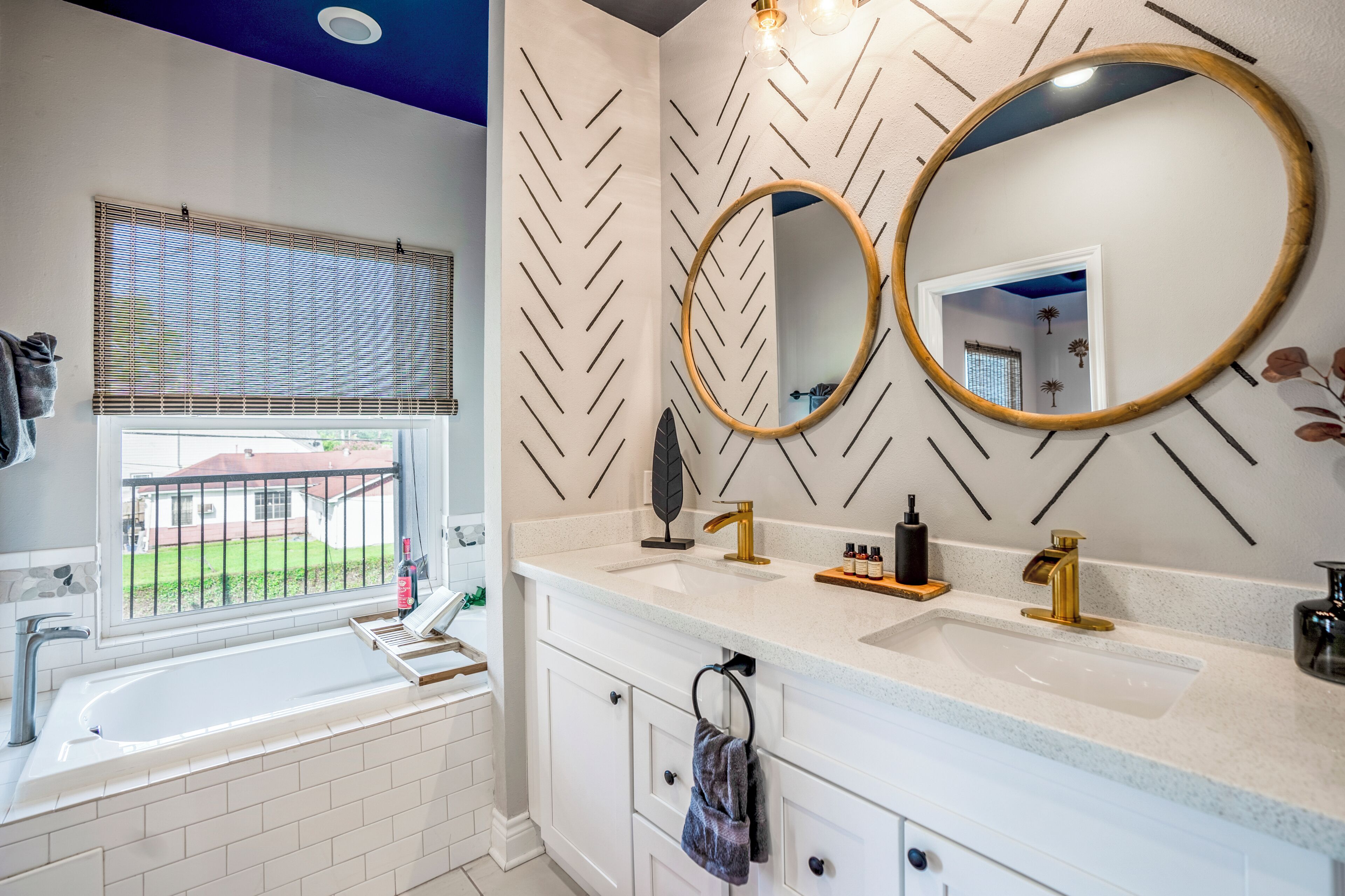 Un baño moderno con un lavamanos grande, dos espejos y una ventana con persianas.