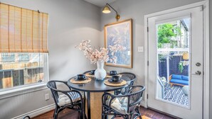 A dining area with a round table, black wicker chairs, a white vase with flowers, and a framed picture on the wall. - Empress Garden Villa (Houston)