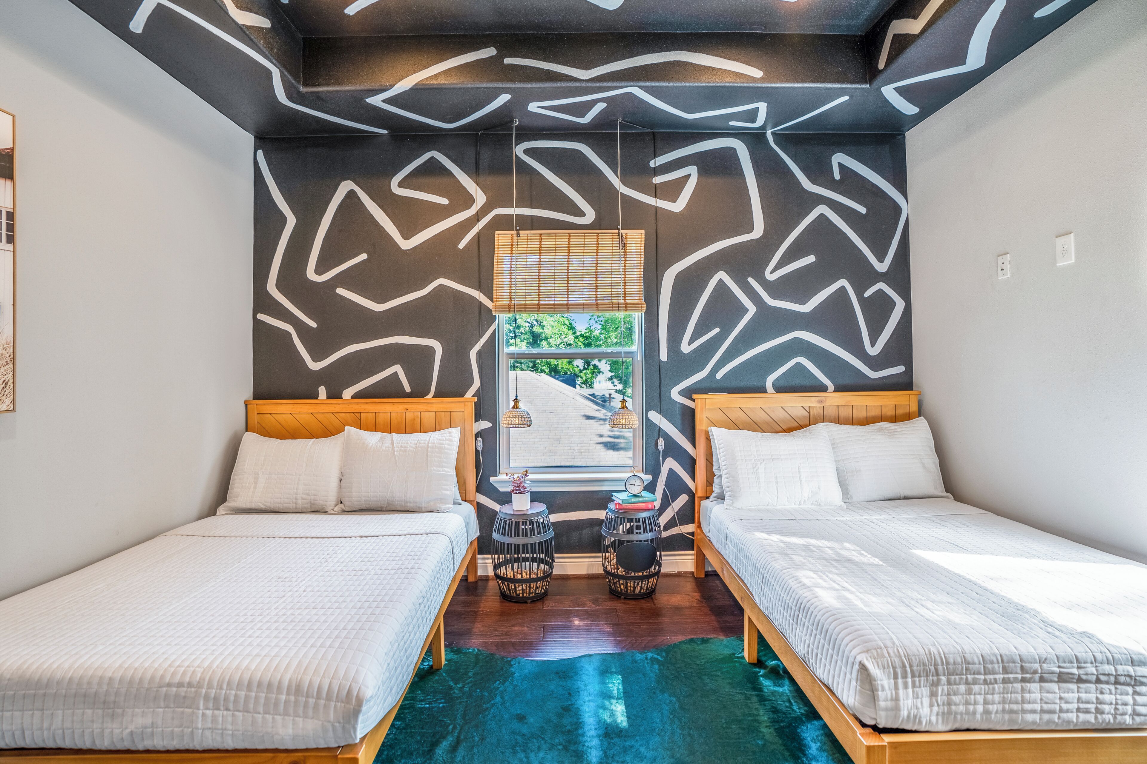 Een kamer met twee bedden, een raam met zonwering, uitzicht op groen buiten en een bijzonder wandontwerp.