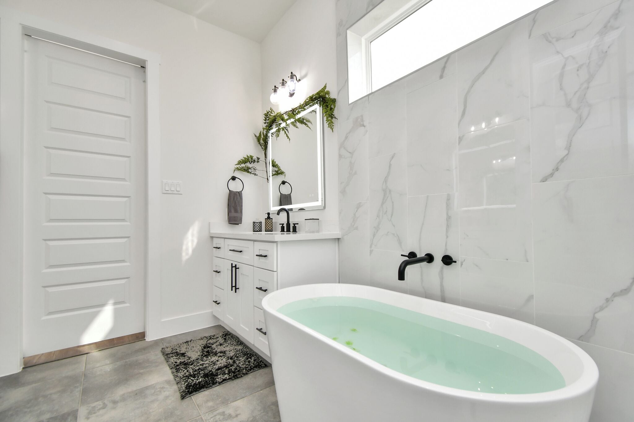 Ein modernes Badezimmer mit einer freistehenden Badewanne, einem weißen Waschtisch mit Spiegel und Marmorwänden.