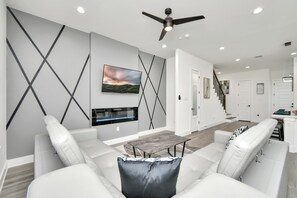Uma sala de estar moderna com sofá, mesa de centro, televisão e ventoinha no teto.