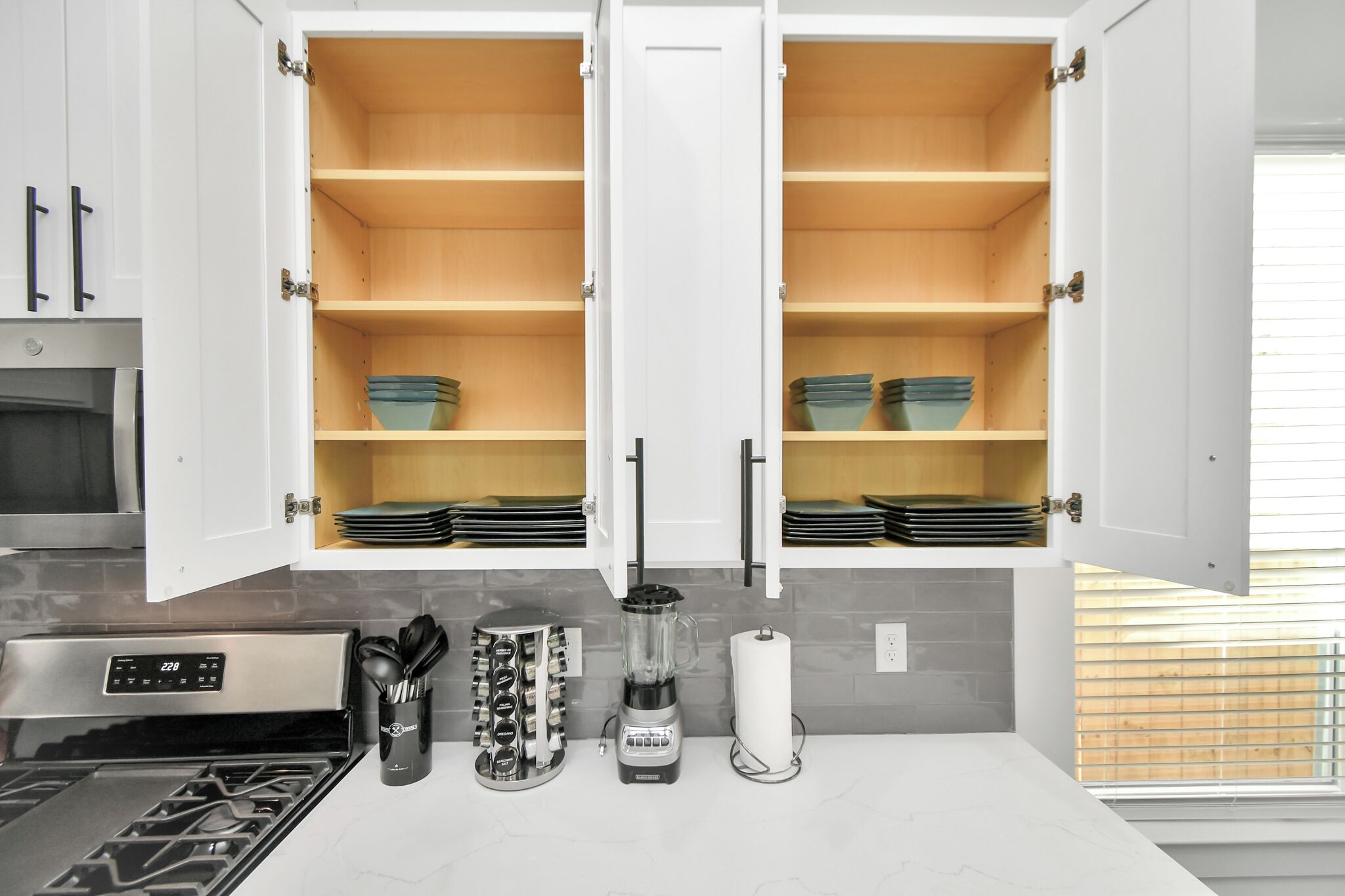 A kitchen with white cabinets, a stove, a blender, and a roll of paper towels.