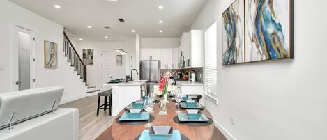 Una cocina moderna con armarios blancos, un refrigerador de acero inoxidable y un comedor con mesa de madera y individuales azules.