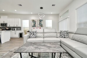 A modern living room with a sectional sofa, a marble coffee table, and a kitchen in the background. - Empress Stylish Retreat (Houston)