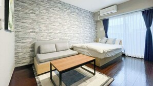 Een kamer met een stenen muur, een bank, een bed, een houten tafel en een raam met gordijnen.