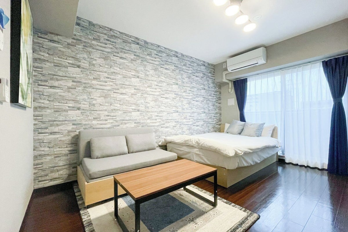 A room with a stone wall, a sofa, a bed, a wooden table, and a window with curtains.