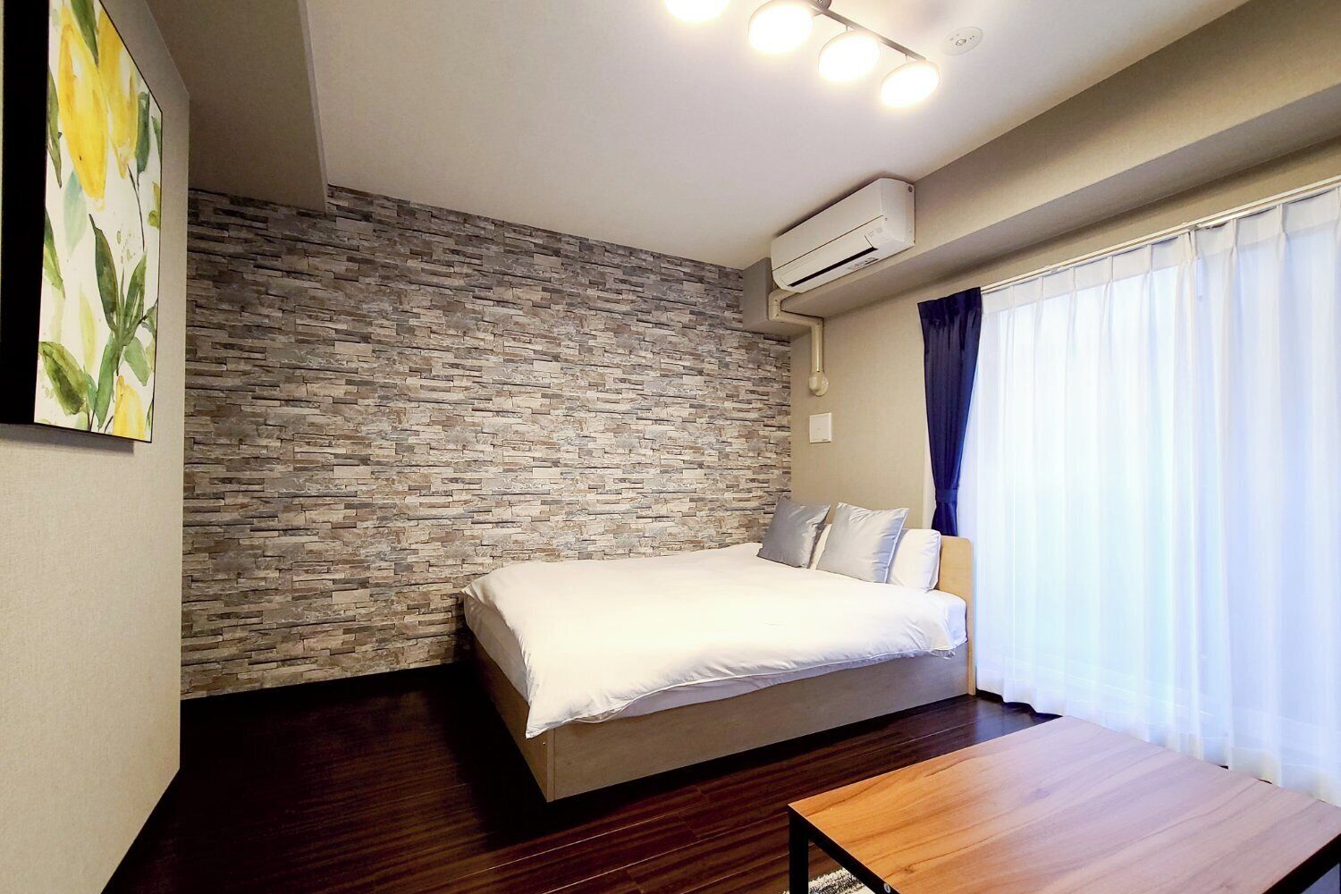 A bedroom with a stone wall, a bed, an air conditioner, and a window with curtains.