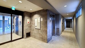 Een moderne hotelgang met glazen deur, nooduitgang, brandalarm en lift.