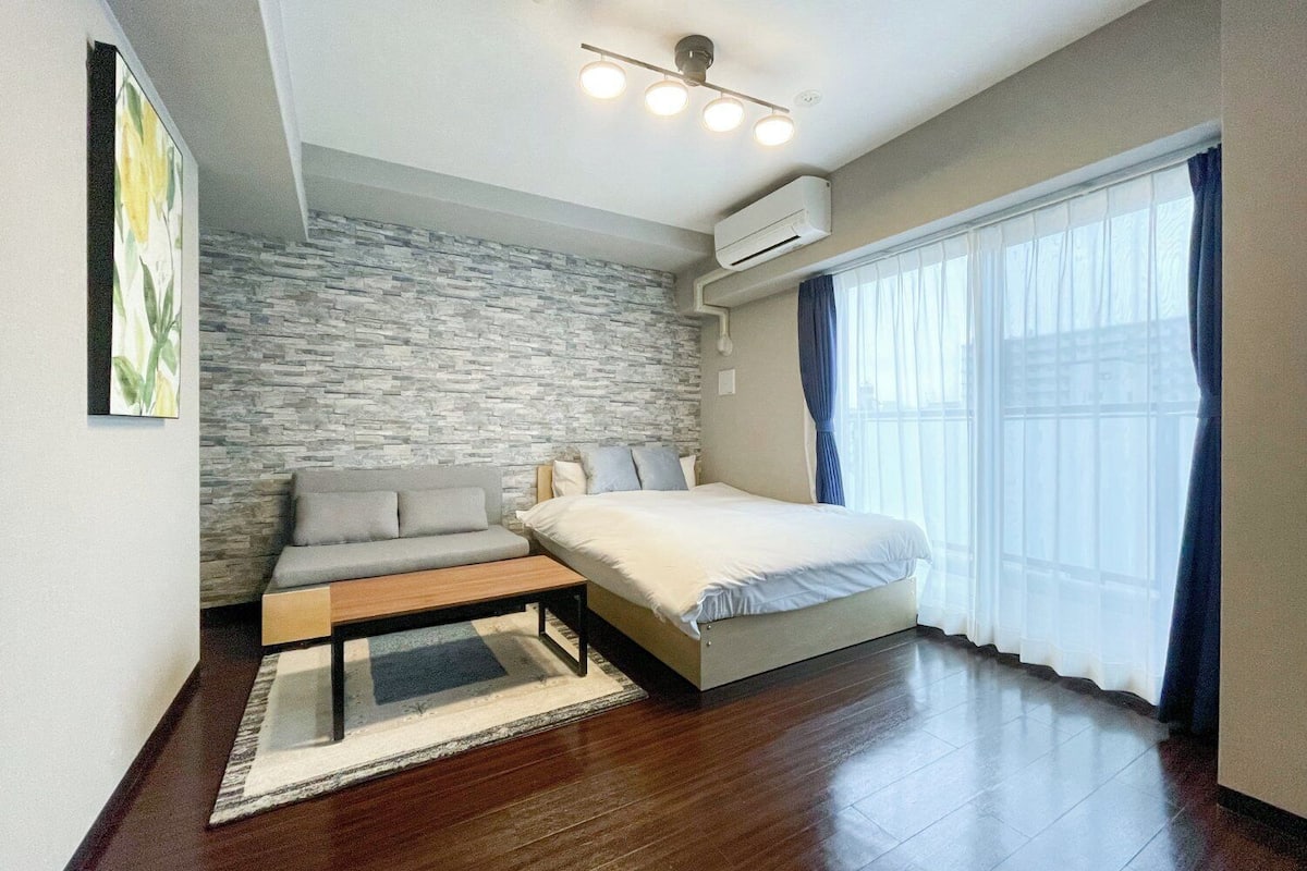 A modern bedroom with a stone wall, a bed, a sofa, and a bench.