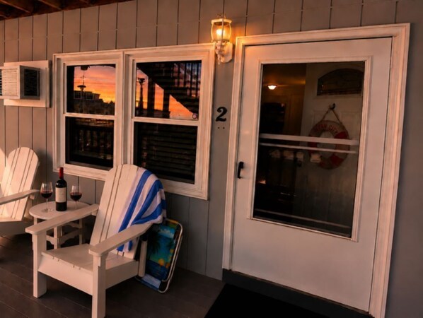 A porch with two white chairs, a small table with a bottle and glass, and a door with a number '2' sign.