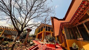 A building with a red staircase leading to a balcony, surrounded by trees and potted plants. - Sinchula Villa Resort (Paro)