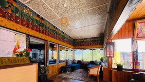 A room with wooden walls, a ceiling with intricate patterns, a reception desk, a sofa, a chair, and a window with a view of greenery. - Sinchula Villa Resort (Paro)