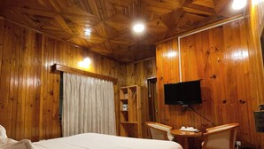 A wooden-paneled room with a bed, a desk, a chair, and a television. - Sinchula Villa Resort (Paro)