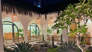 Un patio con mostrador de recepción, ventanales arqueados, luces colgantes y un jardín de rocas.