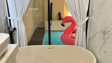 Un bagno moderno con una vasca da bagno indipendente, tende bianche e una decorazione a fenicottero rosso.