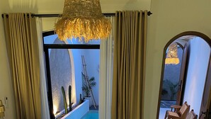Habitación de hotel con cama, vista a una piscina exterior y zona de estar con sillas.