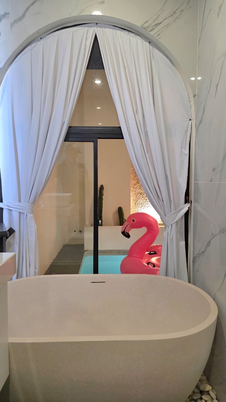 A modern bathroom with a freestanding bathtub, a pink flamingo decoration, and a cactus in the background.