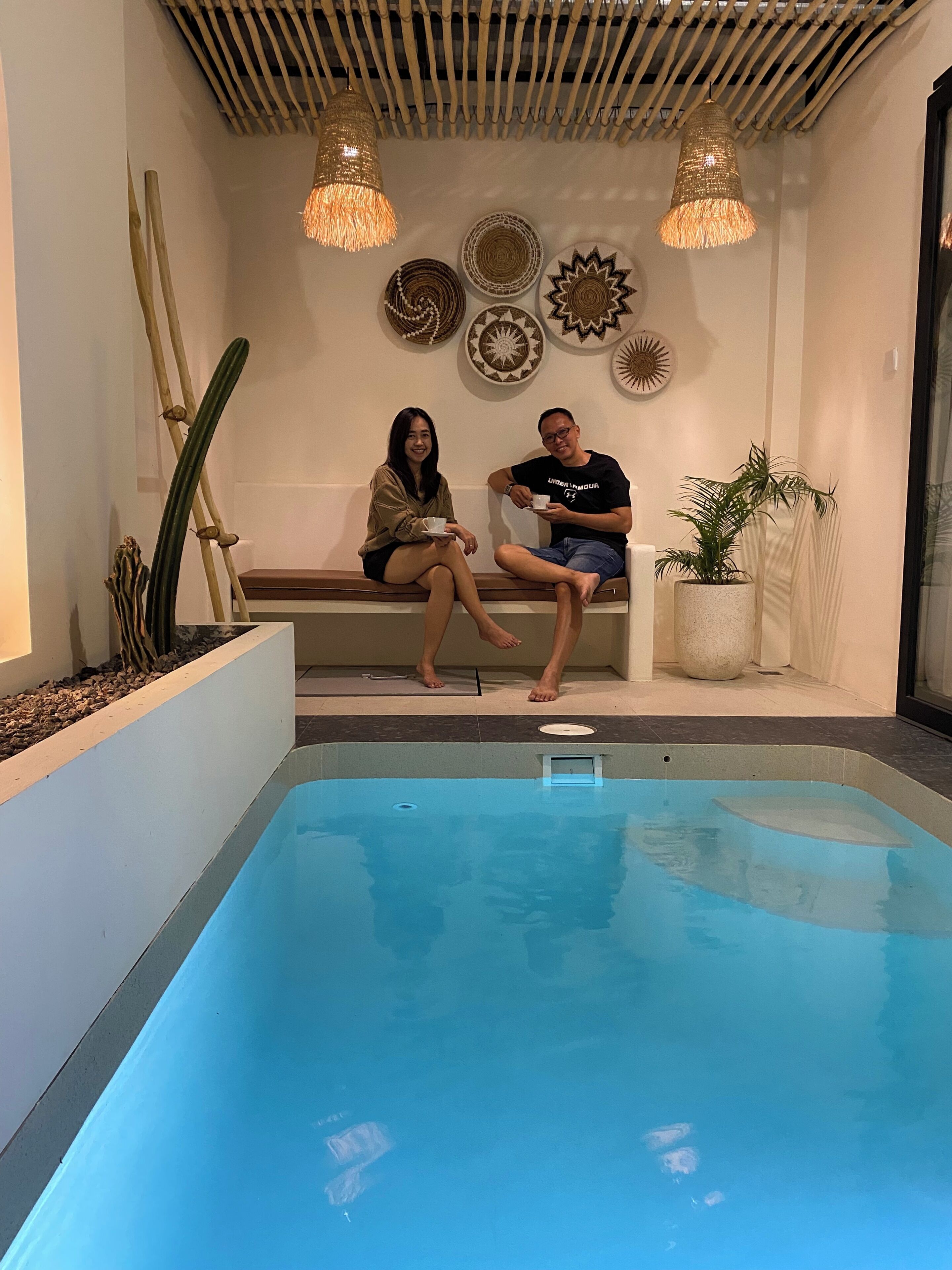 Uma área de piscina com duas pessoas sentadas num banco, teto com design de bambu e placas decorativas na parede.