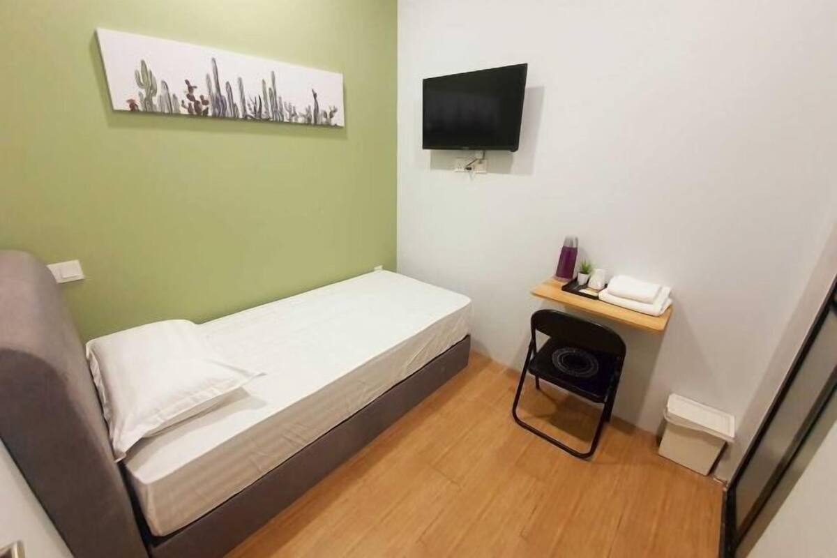 A small room with a bed, a chair, a TV, and a shelf with toiletries.