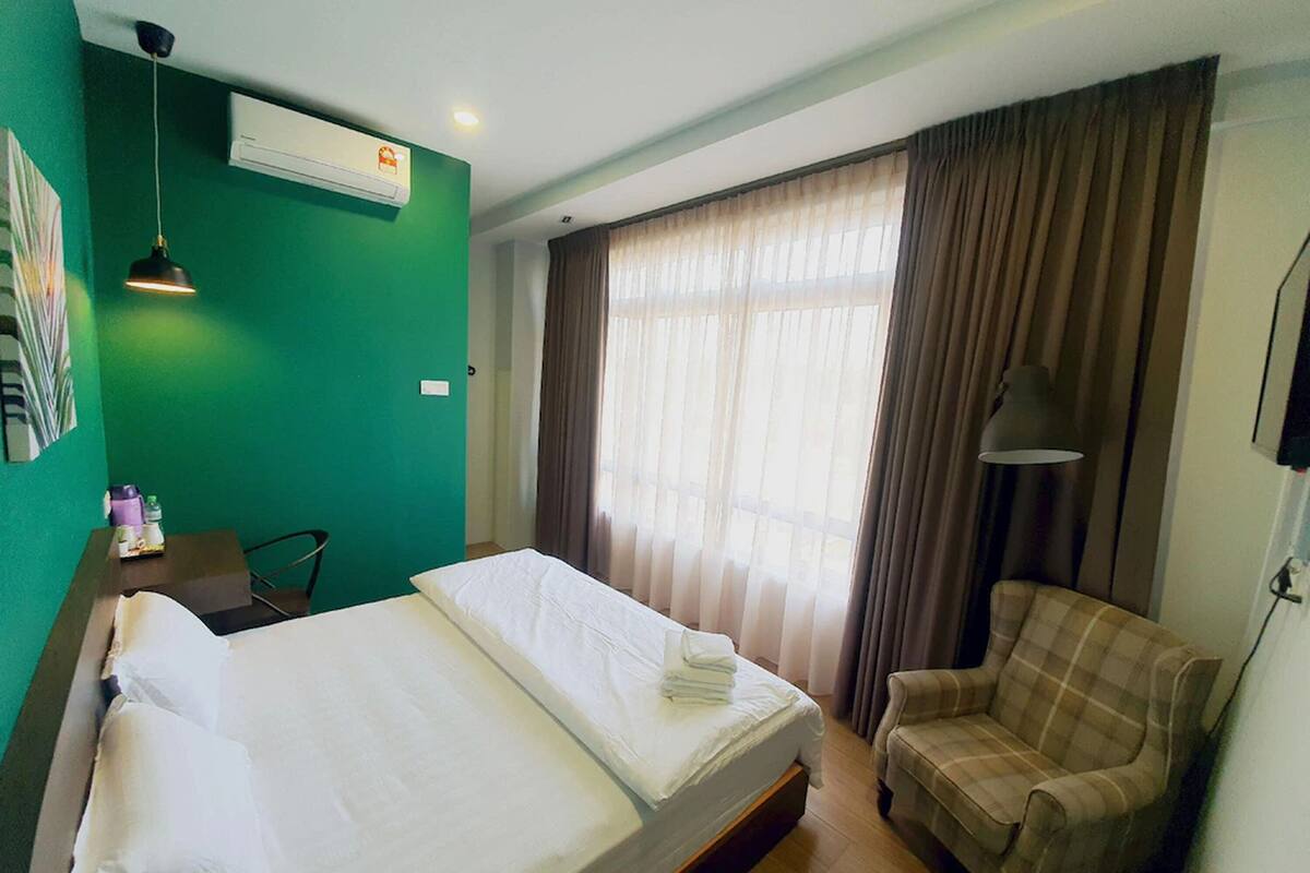A hotel room with a bed, a chair, a desk with a lamp, and a window with curtains.