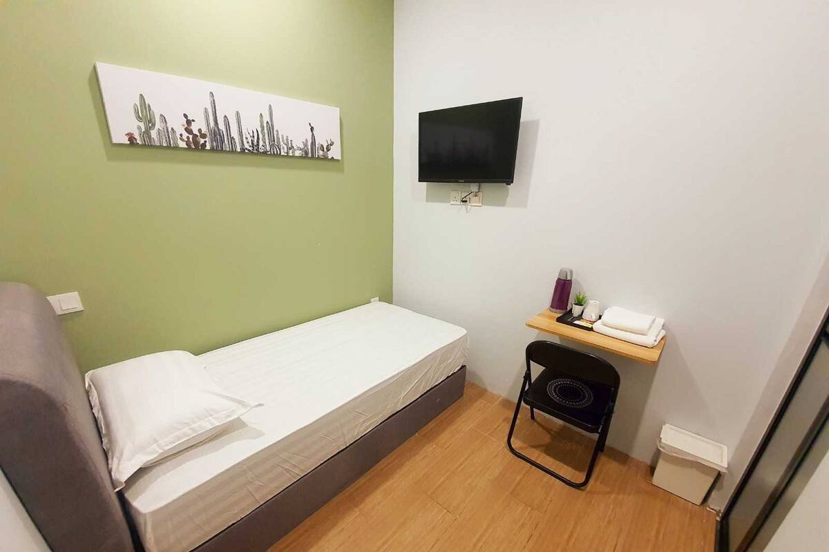 A small room with a bed, a desk with a chair, a flat-screen TV, and a cactus artwork on the wall.