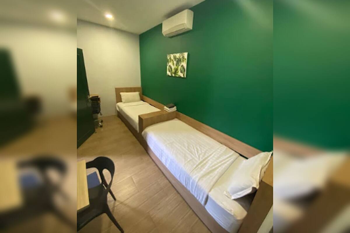 A room with two single beds, a desk, a chair, and a green wall.