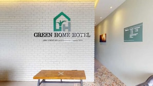A hotel reception area with a white brick wall, a wooden bench, and a green sign listing room and facility names. - HOTEL O OYA INN @ KLIA (Sepang)