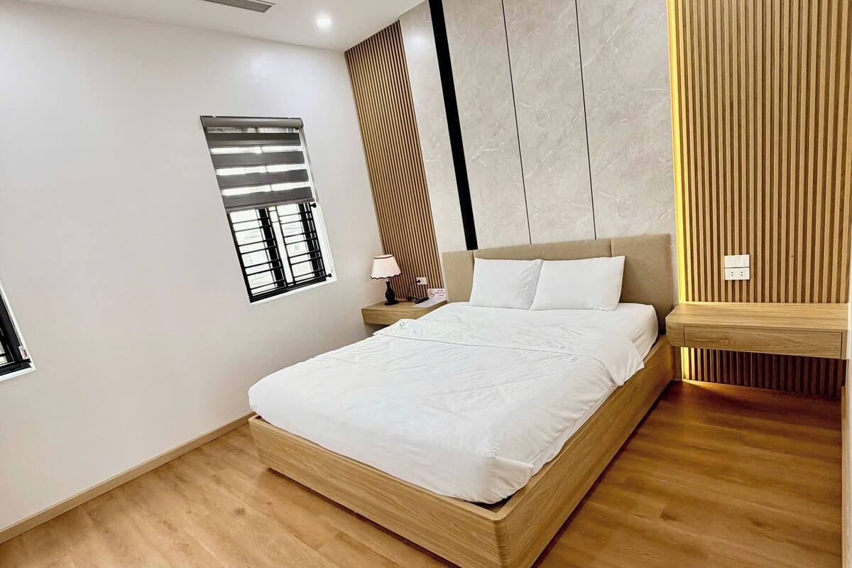 Un dormitorio moderno con una cama de madera, una mesita de noche, un panel en la pared y una ventana con persianas.