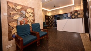 Un área de recepción con una pared de mármol, una estatua, dos sillas azules, un mostrador de recepción y un ventilador de techo.
