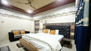 Un dormitorio con cama, sofá, mesita de noche, una pequeña mesa de madera y ventilador de techo.