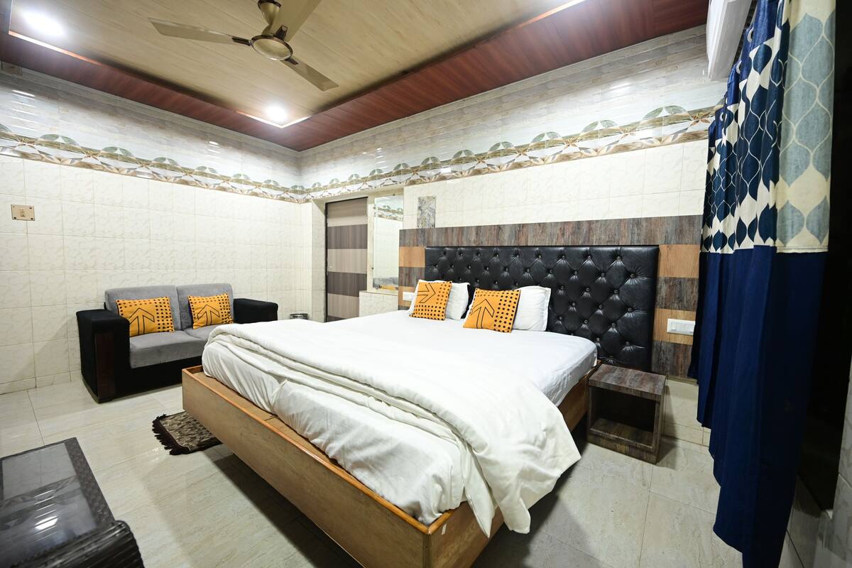 Un dormitorio con cama, sofá, mesita de noche, una pequeña mesa de madera y ventilador de techo.