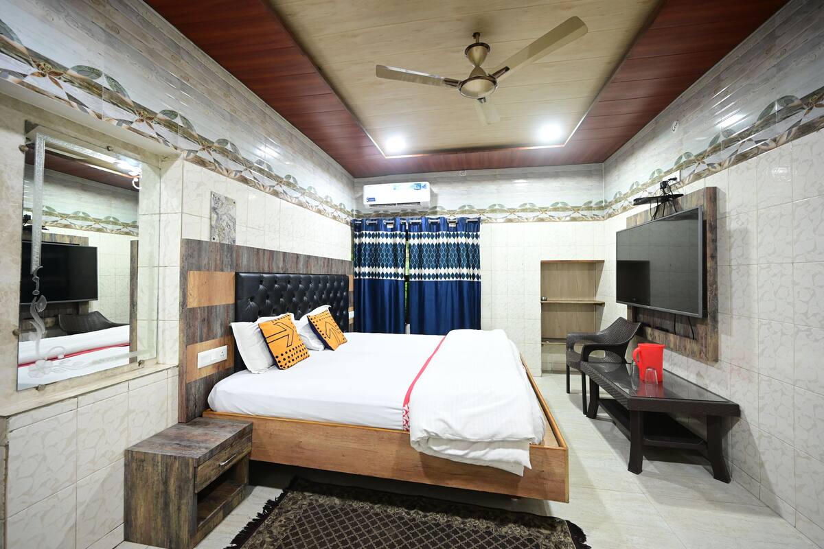 Un dormitorio con cama, televisor, ventilador de techo y ventana con cortinas.