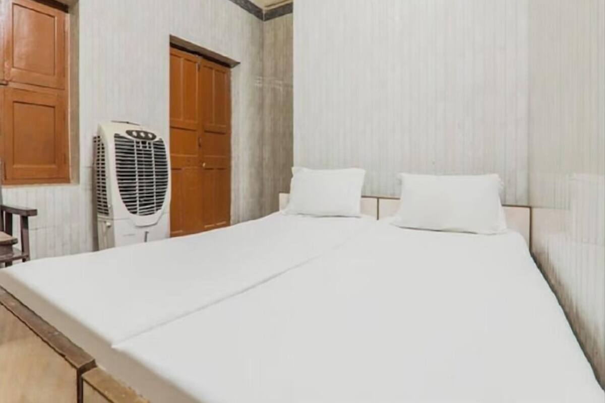 Una habitación de hotel con una cama, dos armarios de madera y un ventilador de pie.