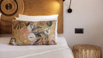 Una cama con un cojín floral, una decoración circular en la pared y un taburete de madera.