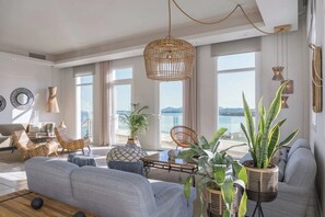 Ein geräumiges Wohnzimmer mit einer großen Couch, einem Couchtisch und Meerblick durch große Fenster.