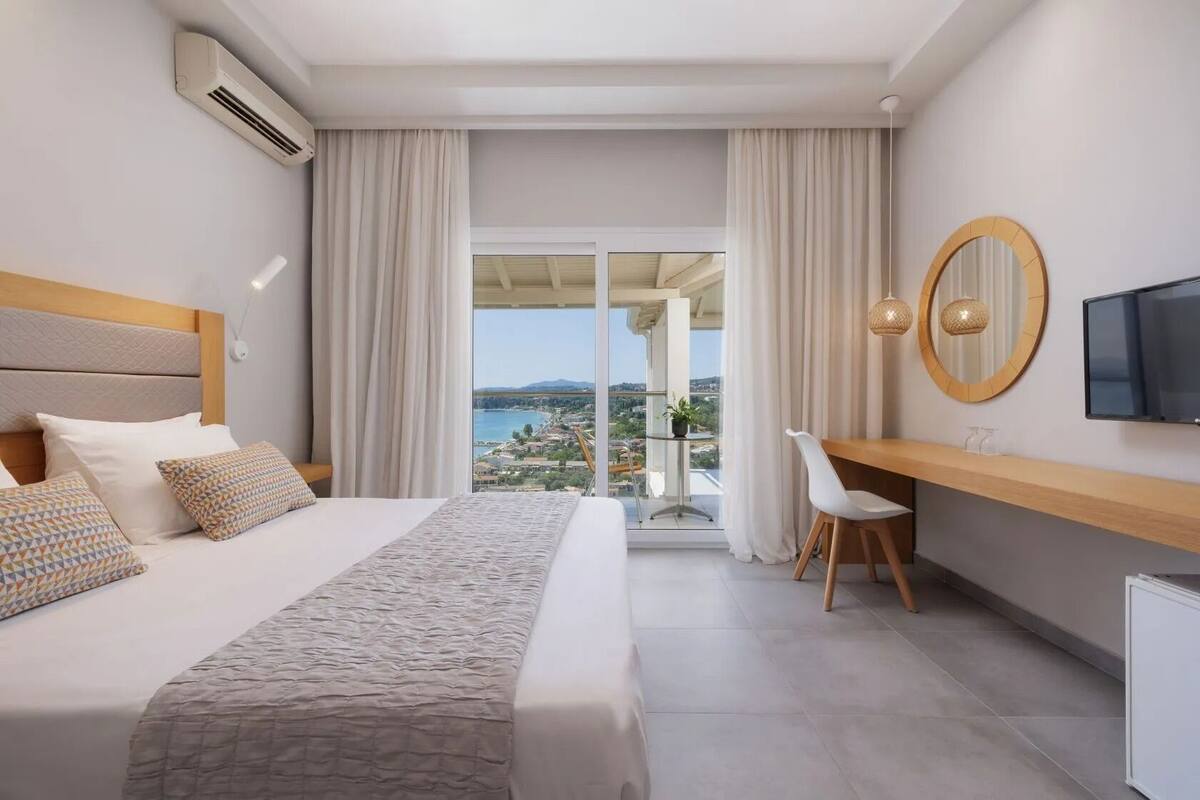 A hotel room with a bed, a desk, a TV, and a view of the city.