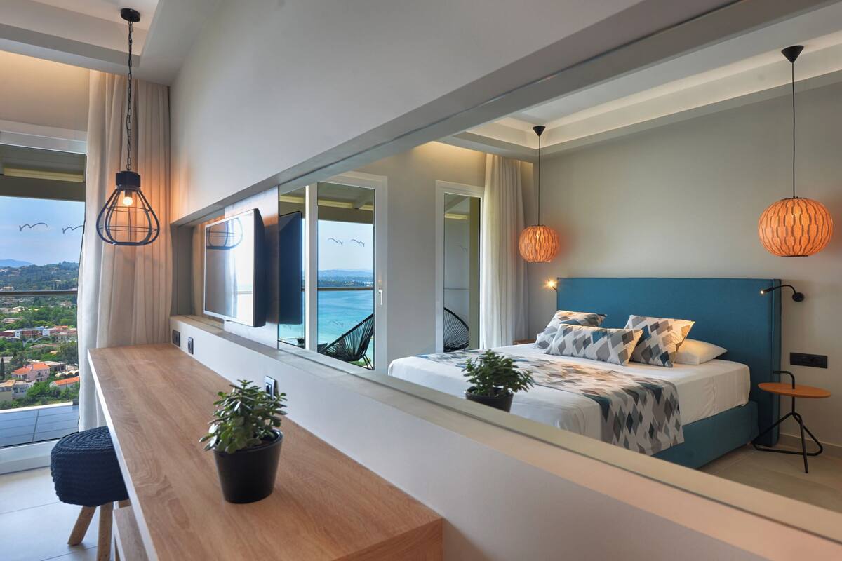 A modern bedroom with a large bed, a wooden desk, and a view of the sea.