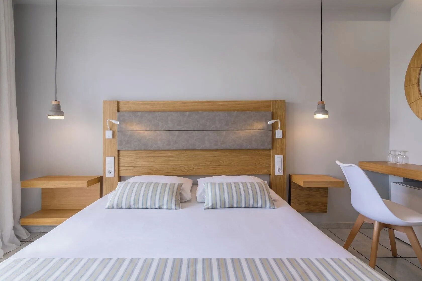 A modern hotel room with a large bed, two bedside tables, a chair, and pendant lights.