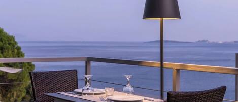 A table set for two with a view of the sea, a black lamp, and wicker chairs.