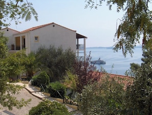 Un edificio frente al mar con balcón, rodeado de vegetación.