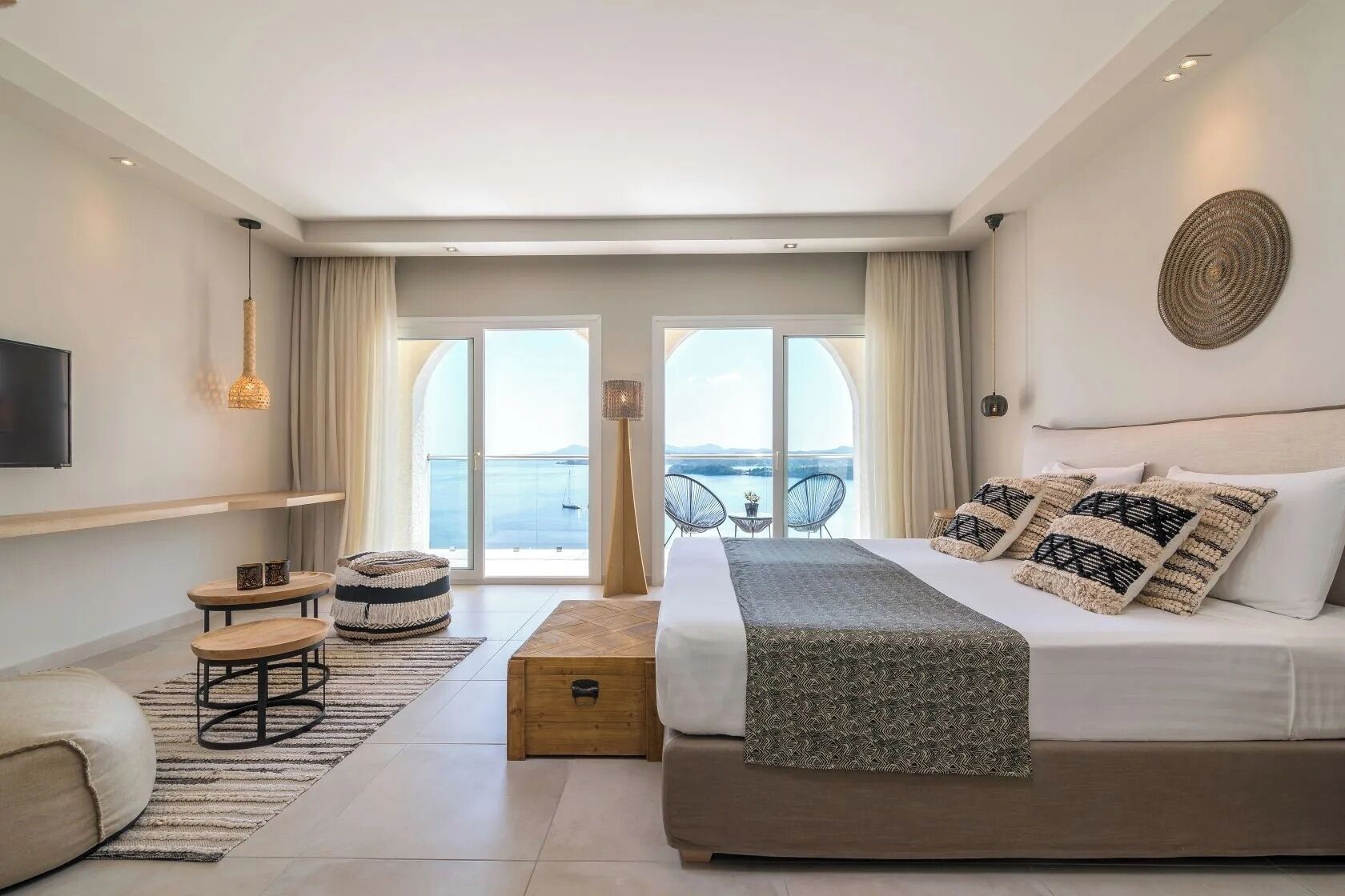 Una camera d'albergo moderna con un letto, un angolo salotto e un balcone con vista.