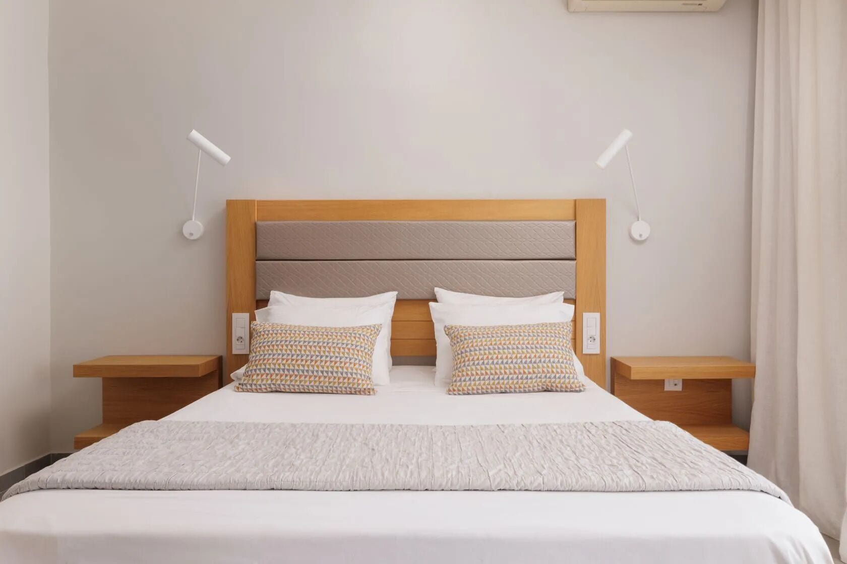 Habitació d'hotel amb un llit, dos coixins, taules de nit i làmpades penjades a la paret.