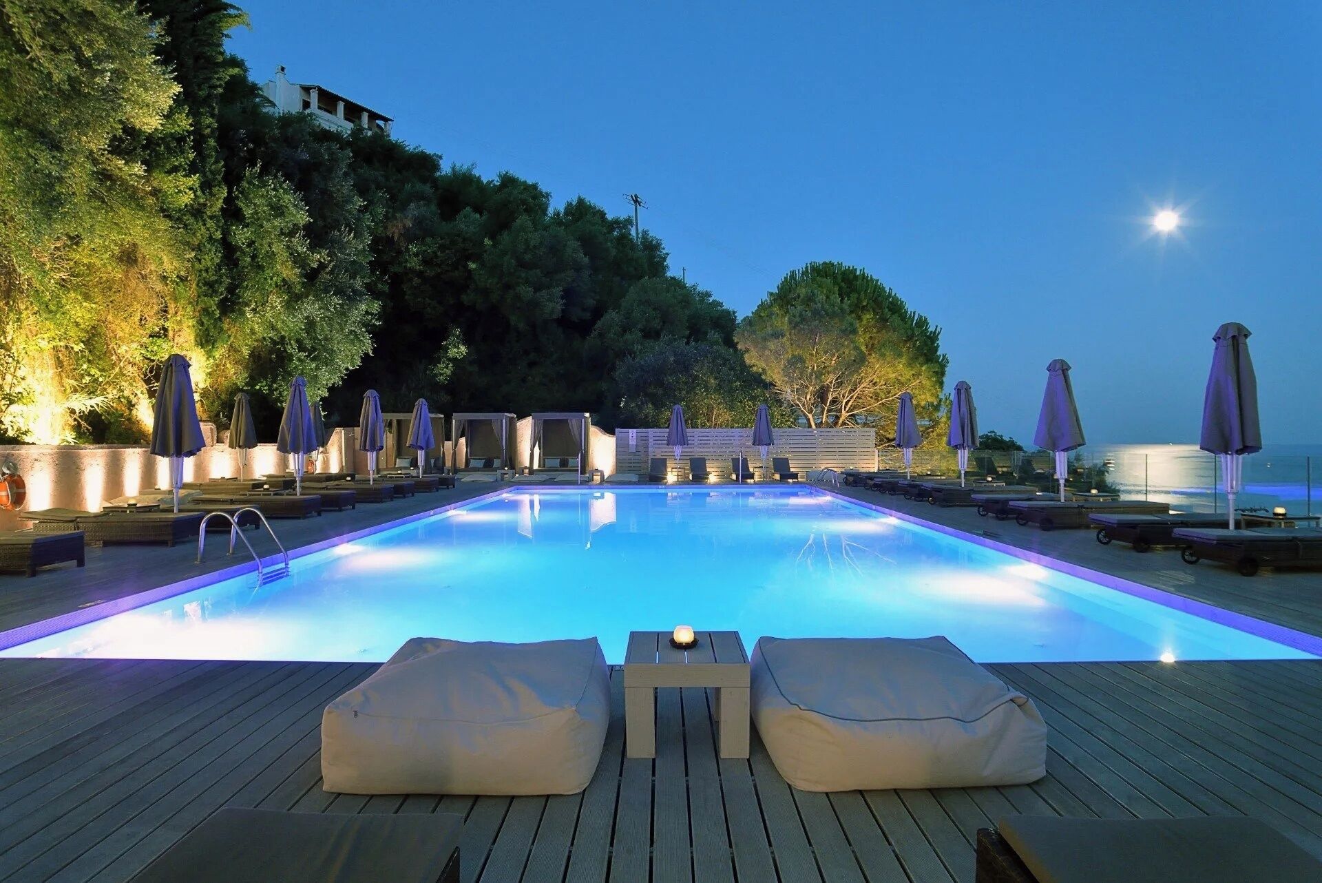 Une piscine entourée d’arbres et dotée d’une terrasse en bois, avec des chaises longues et des parasols.