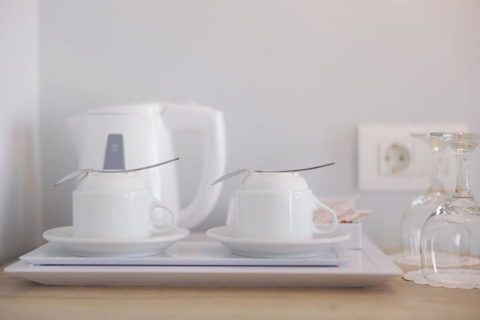 Une machine à café blanche, deux tasses blanches avec des pailles en métal et un plateau sur une surface en bois.