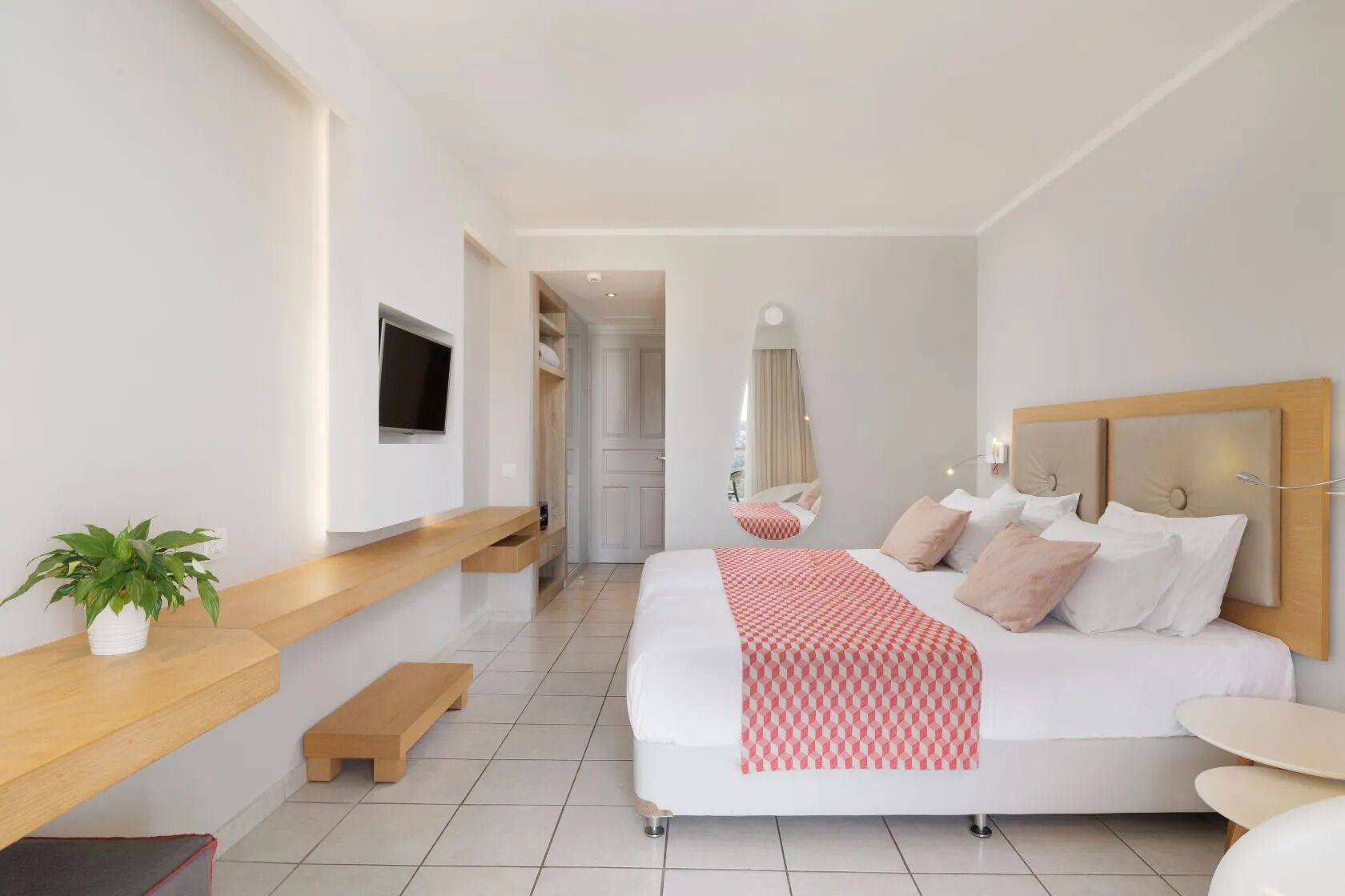 A modern hotel room with a bed, bedside table, TV, and a potted plant.