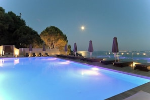A swimming pool with lounge chairs and umbrellas, a wooden deck, and a view of the sea. - Marilena Sea View (Pirgi)