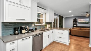 A modern kitchen with white cabinetry, a dishwasher, and a coffee maker. - Empress Solace Villa (Friendswood)